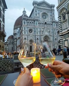 two people holding wine glasses in front of a building with a candle on the table