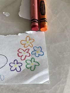 two crayons are next to a piece of paper with flowers drawn on it