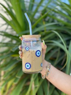 a hand holding a mason jar with an evil eye design on it and a straw