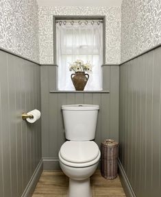 a white toilet sitting in a bathroom next to a window with flowers on the tank