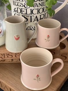 three coffee mugs sitting next to each other on a wooden tray with a plant in the background