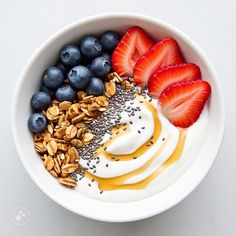 a bowl filled with yogurt, strawberries and blueberries next to granola