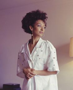 a woman standing in front of a lamp wearing a white shirt and silver hoop earrings