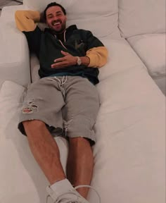 a man laying on top of a white couch with his arms around his head and legs crossed