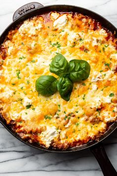 a cheesy casserole with basil leaves on top sits in a cast iron skillet