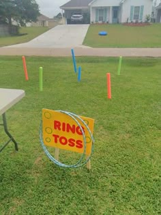 a ring toss sign sitting on top of a lush green field next to a white table