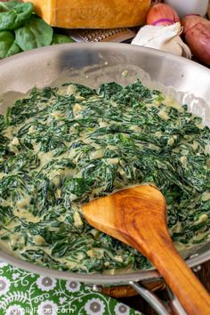 spinach and cheese in a pan with a wooden spoon on the table next to it