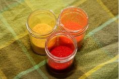 three jars filled with different colored powders on top of a plaid tablecloth covered floor