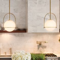 two lights hanging over a kitchen counter with flowers in the vases on the counter