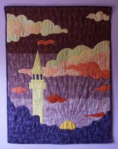 a quilted wall hanging with a castle in the sky and clouds on it's side