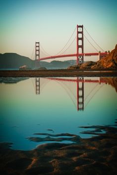 the golden gate bridge in san francisco, california is reflected in the water at sunset