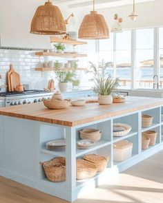 a kitchen island with baskets on it and hanging lights over the top, in front of an open window