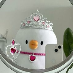 a mirror with a penguin wearing a tiara and holding a cell phone in front of it