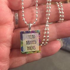 a hand holding a small square pendant with the words i read dainty books on it