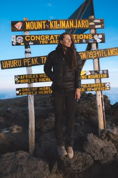 a woman standing on top of a mountain with lots of signs in front of her