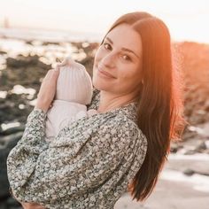 a woman holding a baby in her arms on the beach at sunset or sunrise time