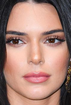 a close up of a woman with dark hair and brown eyes, wearing gold jewelry