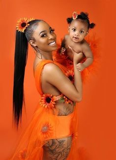 a woman holding a baby wearing an orange outfit with sunflowers on her chest