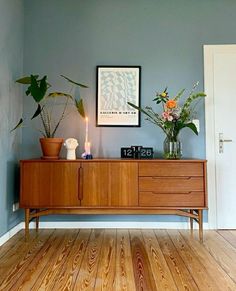 a living room with blue walls and wooden floors, two potted plants on top of a dresser