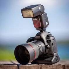 a camera with a flash light attached to it's body sitting on top of a wooden fence