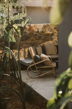 a chair sitting on top of a cement floor next to a stone wall and plants