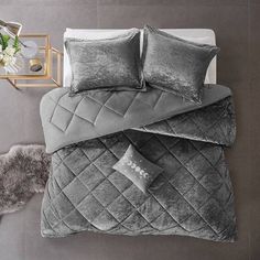 a bed with grey sheets and pillows on it