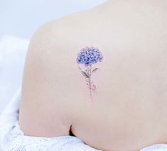 the back of a woman's shoulder with a small blue flower tattoo on it