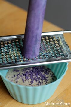 a purple candle sitting on top of a blue cup filled with lavender sprinkles