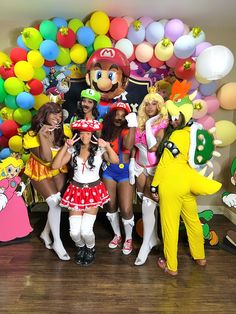 several people dressed up in costumes posing for a photo with balloons and characters behind them