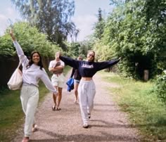 two women walking down a dirt road with their arms in the air and one holding her hands up