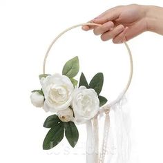 a hand holding a white flower in a hoop with greenery on the top and bottom