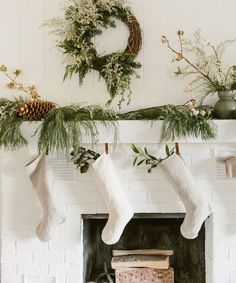 christmas stockings hanging from the mantel with greenery and pine cones on it, next to a wreath