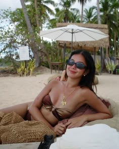 a woman laying on top of a sandy beach next to palm trees and umbrellas