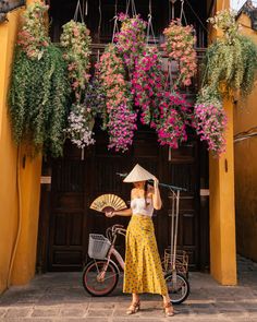 a woman standing in front of a yellow building with flowers hanging from it's roof