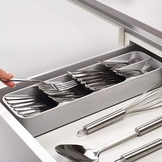 a person is reaching for silverware in a stainless steel drawer with utensils and spoons