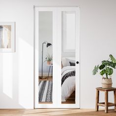 a bedroom with white walls and wooden floors, two plants in vases on the floor