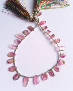 a necklace with pink beads and tassels hanging from it's side on a white surface