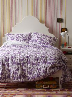 a bed with purple and white bedspread on top of it next to a nightstand