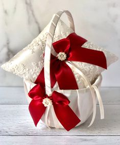 a white basket filled with red ribbon and bows on top of a wooden table next to a pillow