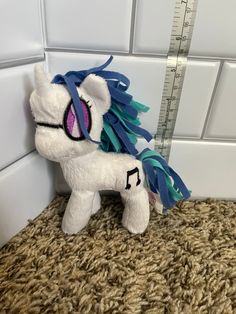 a white stuffed pony with blue manes next to a ruler