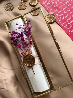 an open box with some flowers in it on top of a pink sheet and gold foil