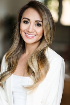 a woman with long hair wearing a white blazer and posing for a photo in front of