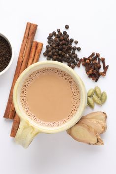 a cup of coffee surrounded by cinnamon, cloves and other spices on a white surface