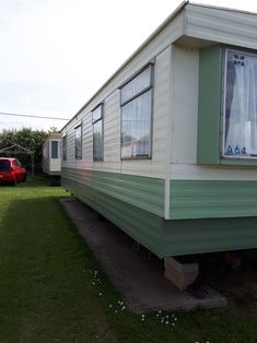 a green and white mobile home sitting on top of a lush green field next to a red car