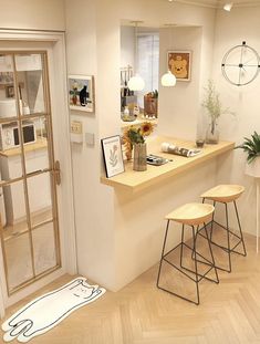 a room with two stools and some pictures on the wall above it, in front of an open door