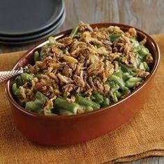 a bowl filled with green beans and nuts on top of a wooden table next to plates