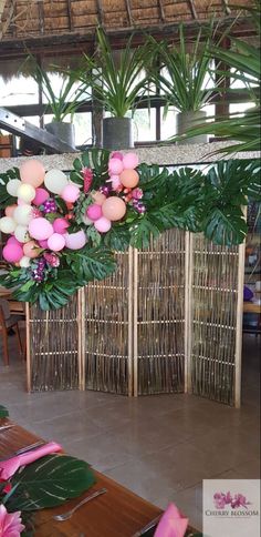 an arrangement of flowers and greenery is displayed in front of a bamboo screen divider