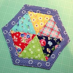 a close up of a patchwork quilt on a table with green cloth and blue background