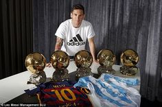 the soccer player is posing with his trophies and balls in front of him on a table