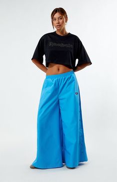 Stay effortlessly cool with these Reebok Angel Wide Leg Track Pants. Crafted from recycled fabric, they feature a low-rise, elastic waistband, side hand pockets, and snap-button details, all complemented by Reebok's soft-touch logo for a relaxed fit with wide-leg openings.13" rise28" inseam40" leg openingsSolid color track pantsLow-riseElastic waistbandSide hand pocketsSnap-button side detailsReebok soft-touch logoWide leg openingsRelaxed fit100% recycled polyesterMachine washableModel is wearing a size smallModel measurements: 5’9” height, 32” bust, 25” waist, 34” hipsMeasurements taken from a size smallLearn more about PacSun eco items Reebok Womens Angel Wide Leg Track Pants - Blue size Small Blue Workout Bottoms With Elastic Side Panels, Blue Sportswear Bottoms With Elastic Side Panels, Blue Relaxed Fit Workout Pants, Blue Workout Bottoms With Ribbed Waistband, Spring Moisture-wicking Cotton Bottoms, Blue Wide Leg Sports Bottoms, Sports Wide Leg Bottoms With Elastic Side Panels, Blue Wide Leg Athleisure Activewear, Blue Streetwear Bottoms With Elastic Side Panels